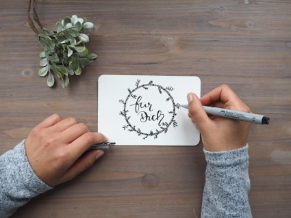 Eine Hand zeichnet einen Blumenkranz mit einem Schriftzug "für Dich".