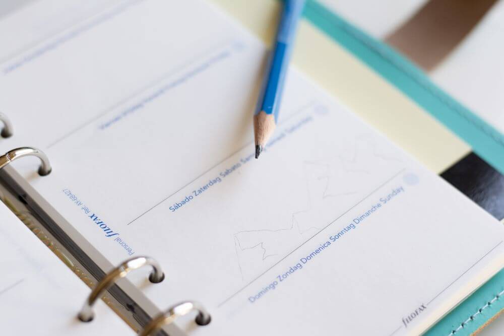 Ein aufgeschlagener Kalender von Filofax liegt auf dem Tisch. In ihm ist eine Bergkette mit Bleistift skizziert.