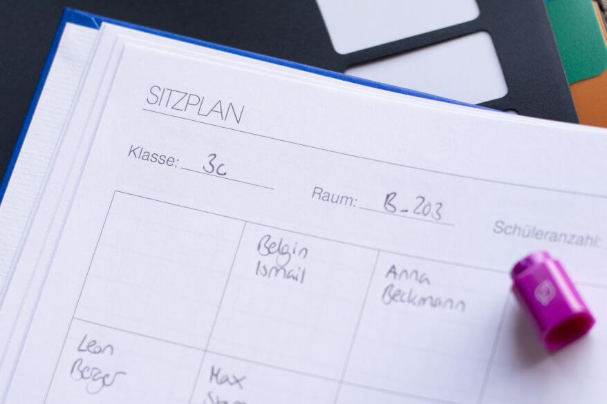 Ein Lehrerkalender liegt aufgeschlagen auf einem Tisch. Es ist ein Teil eines Sitzplans zu sehen. 