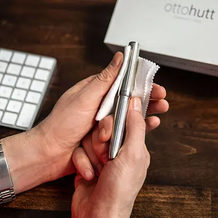 Jemand poliert einen silbernen Füller von Otto Hutt vor einem Holzschreibtisch mit einem weißen Tuch.