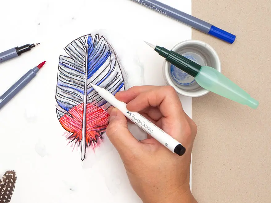Jemand malt mit einem weißen Pigmentliner Highlights auf eine gezeichnete und aquarellierte Vogelfeder in Blau- und Rottönen. Foto: Johanna Rundel