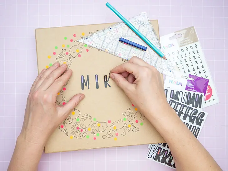 Jemand klebt mit Buchstabenaufklebern von HEYDA den Namen "Mika" auf den Deckel einer Pappschachtel von KNORR prandell. Foto: Johanna Rundel