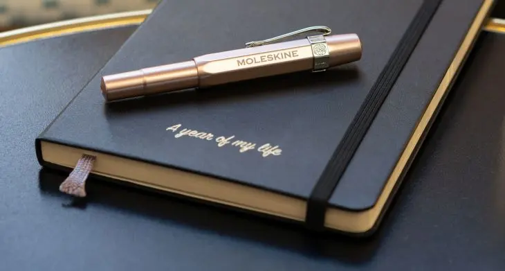 Auf einem schwarzen Kalender von Moleskine liegt ein Füller mit dem eingravierten Wort „Moleskine“.