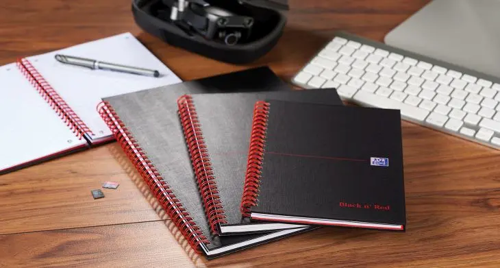 Auf einem Schreibtisch liegen neben Tastatur und Headset mehrer Notizbcher „Black ans red“ von Oxford