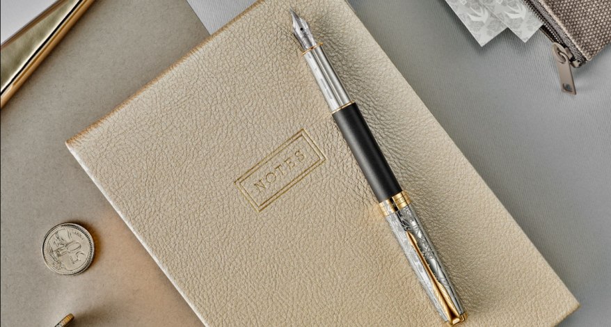 Ein Füller der Marke Parker liegt auf einem cremefarbenen Notizbuch.