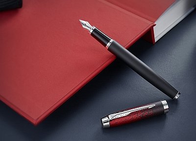 Ein schwarz-roter Füller von Parker lehnt an einem roten Buch.