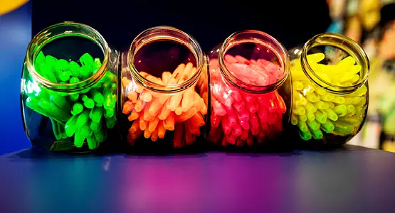 In vier Aufbewahrungsgläsern liegen farblich sortiert Stifte in grün, orange, pink und gelb.