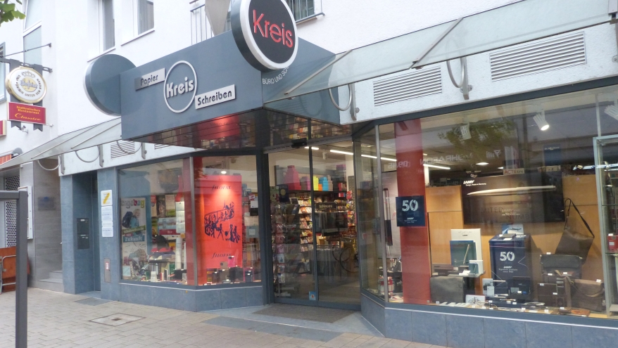Sicht von Außen in das Fachgeschäft Papier Kreis. Die Fenster sind mit Arbeitstaschen und zahlreichen Büroutensilien dekoriert.