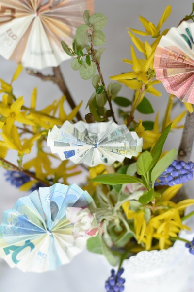 Nahaufnahme gefalteter Geldscheine zu einer runden Blüte in einem Blumenstrauß