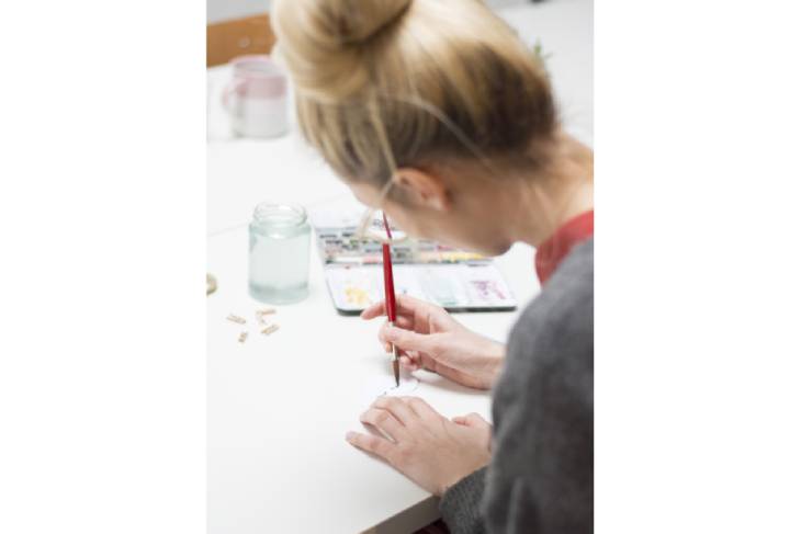 Frau malt mit feinem Pinsel an DIY-Projekt mit Aquarellfarben