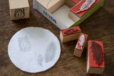 Weißer runder Filz mit gestempelten Eulen- und Feder-Motiven, daneben liegen die Stempel