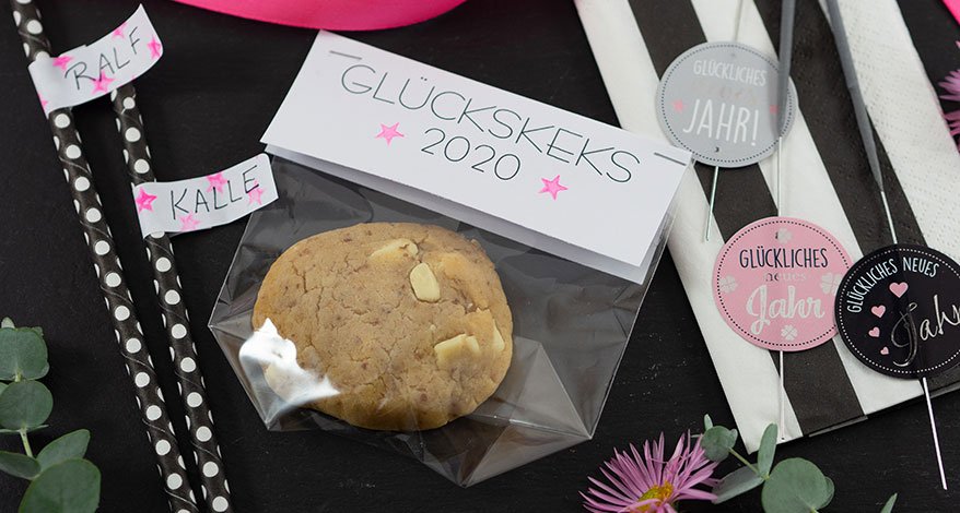 Keks in Tüte mit Etikett „Glückskeks 2020“, drumherum Silvester-Deko