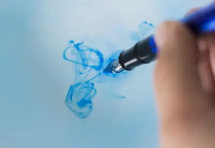 Die Federspitze eines Füllfederhalters wird in Wasser getunkt, welches dann blaue Schlieren zieht.