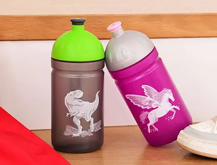 Eine graue Trinkflasche mit grünem Deckel und Dino-Motiv und eine pinke Trinkflache mit grauem Deckel und Einhornmotiv stehen nebeneinander auf einer Treppenstufe. Beide sind aus Plastik und von Step by Step