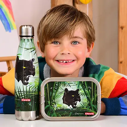 Ein Junge im Grundschulalter in einem Regenbogenfarben-gestreiften Pullover sitzt hinter seiner Brotdose und Trinkflaschen mit Panther-Motiv von Step by Step und grinst in die Kamera.