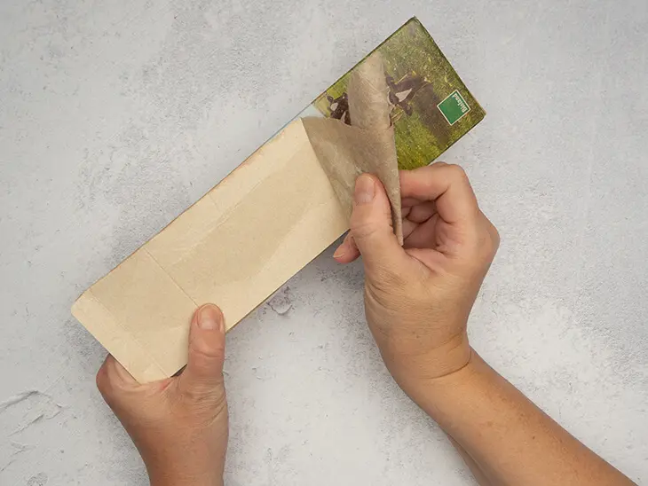 Jemand zieht die oberste Papierschicht von einer aufgeschnittenen Milchtüte ab.