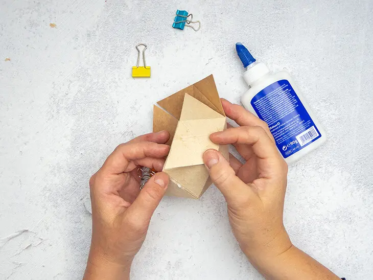 Jemand klebt eine geometrische Form aus einer Milchtüte zu einem Blumentopf zusammen.