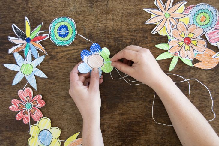 Jemand fädelt bunt bemalte Papierblumen auf einer Kordel auf.