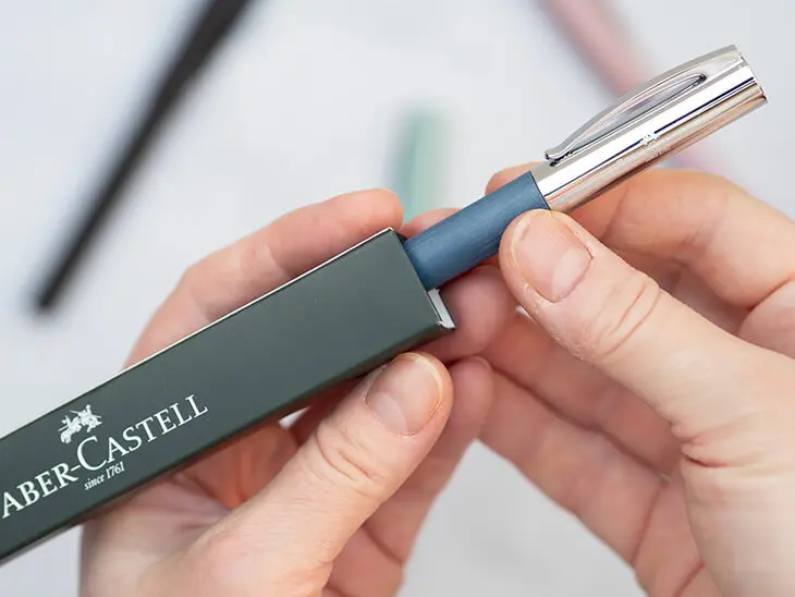 Jemand zieht einen blauen Füller von Faber-Castell aus einer grünen Verpackung. Foto: Johanna Rundel
