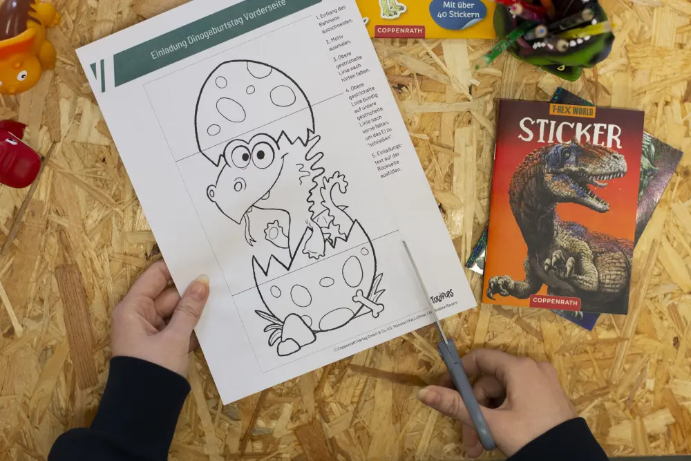 Jemand schneidet eine Vorlage für eine Kindergeburtstagseinladung mit dem Drachen Furzipups aus
