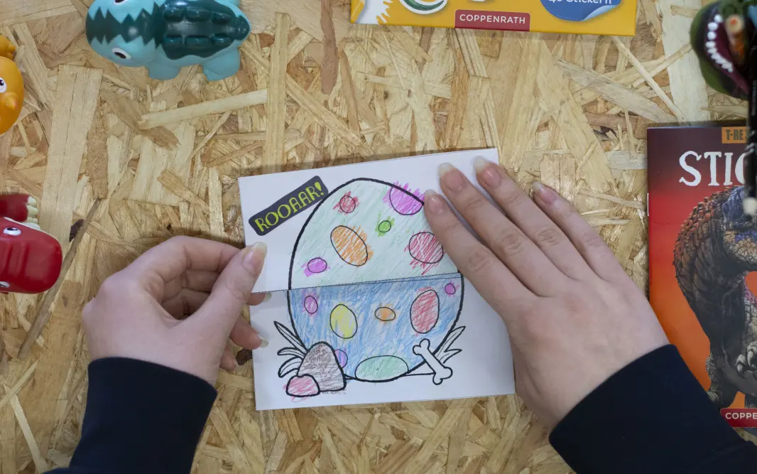 emand faltet eine Vorlage für eine Kindergeburtstagseinladung mit dem Drachen Furzipups zu einem Drachenei zusammen