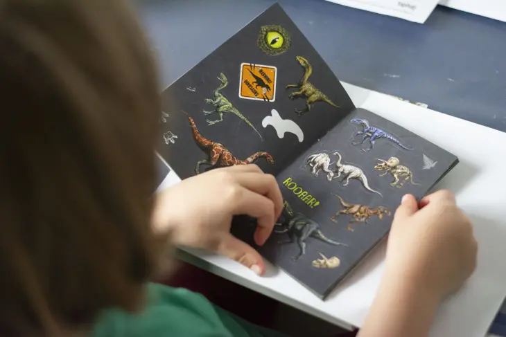 Ein Kind blättert in einem Dino-Stickerbuch von Coppenrath