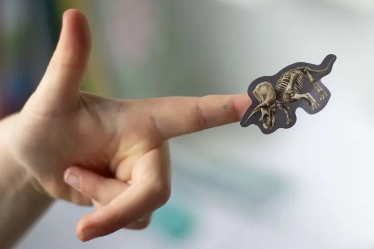 Auf einem Kinderfinger klebt ein Sticker von einem Triceratop-Skelett