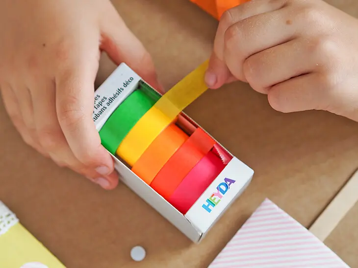 Ein Kind rollt buntes Washitape von einem Spender von HEYDA ab. Foto: Johanna Rundel