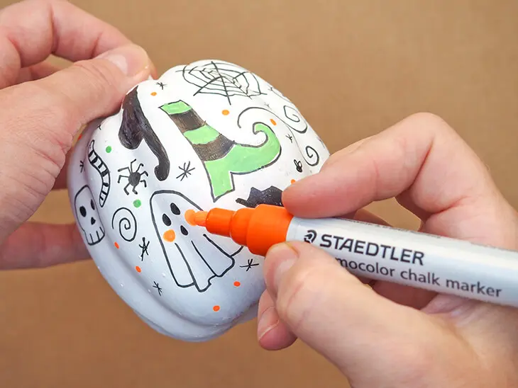 Jemand bemalt einen Kürbis mit einem fluoreszierenden Chalk-Marker von STAETDLER. Foto: Johanna Rundel