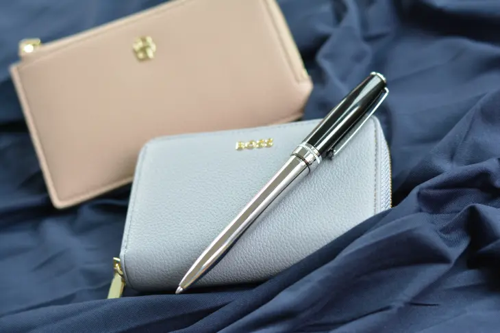 Ein Kugelschreiber von HUGO BOSS liegt mit Börse und Kartenmäppchen auf blauem Satin