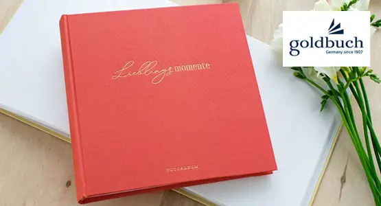 Ein rotes Fotoalbum und Blumen liegen auf einem Tisch. 