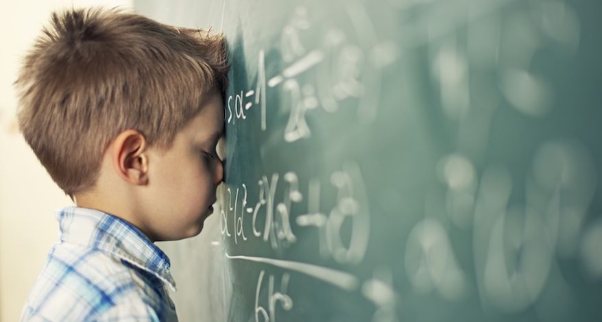 Ein Junge steht vor einer mit Formeln beschriebener Tafel und lehnt mit geschlossenen Augen den Kopf und die Nase an die Tafel.