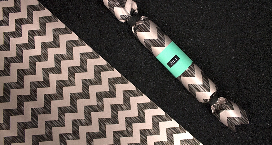 Nahaufnahme eines rollenförmigen Geschenks, welches in schwarz-goldenes Papier eingepackt ist. Es ist mit einem türkisen Aufkleber verziert, auf dem der Name Jule steht.