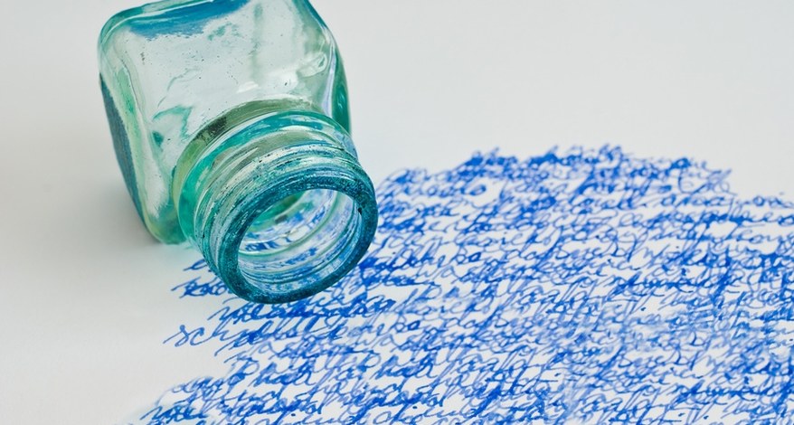 Auf einem Blatt Papier sind mit blauer Tinte ganz viele Kringel gezeichnet. Ein leeres Tintenglas liegt umgekippt auf dem Papier.