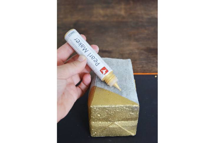 Ein Betonbecher, der mit einer goldenen Ecke besprüht ist, wird mit weiterer goldener Farbe verziert.