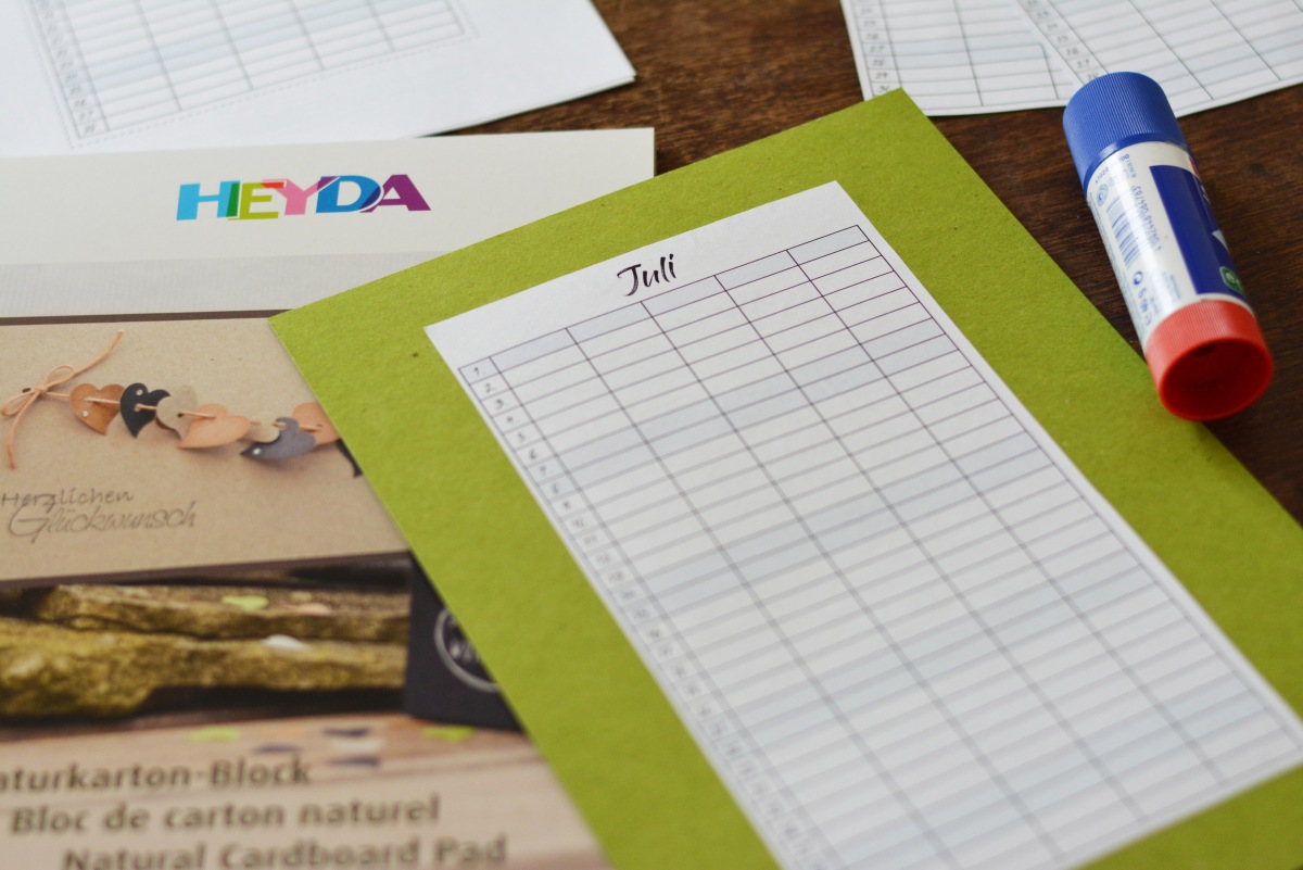 Jahresplaner mit Monatsblatt Juli auf grünem Karton und Klebestift.