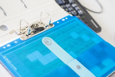 Ringordner mit blauer Hülle und Dokument auf Schreibtisch neben Tastatur.