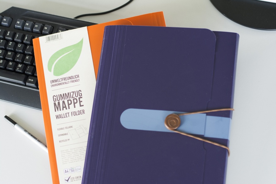 Gummizugmappen aus umweltfreundlichem Material in Lila und orange auf Tisch.