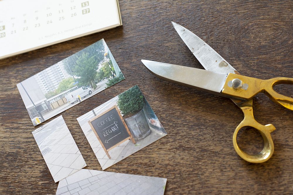 Auf einem Tisch liegen zugeschnittene Fotos, eine Schere und ein BAstelkalender von Heye.