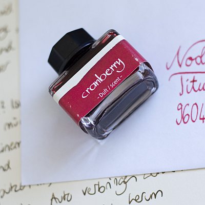 Tintenflasche mit Dufttinte „Cranberry“ auf handbeschriebenem Papier.