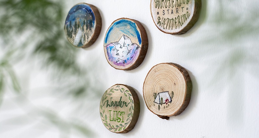Handgemalte Baumscheiben mit Berg-, Wald- und Campingmotiven an der Wand