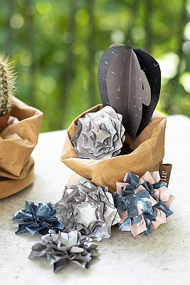 Papiersukkulente und gebastelte Papierblumen in rosa, silber und blau auf einem Tisch