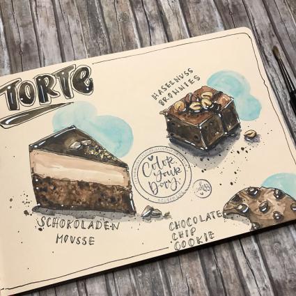 In das Toned Watercolour Book von Hahnemühle wurden verschiedene Kuchen mit Aquarellfarbe gemalt. Das Buch liegt auf einem Holzboden.