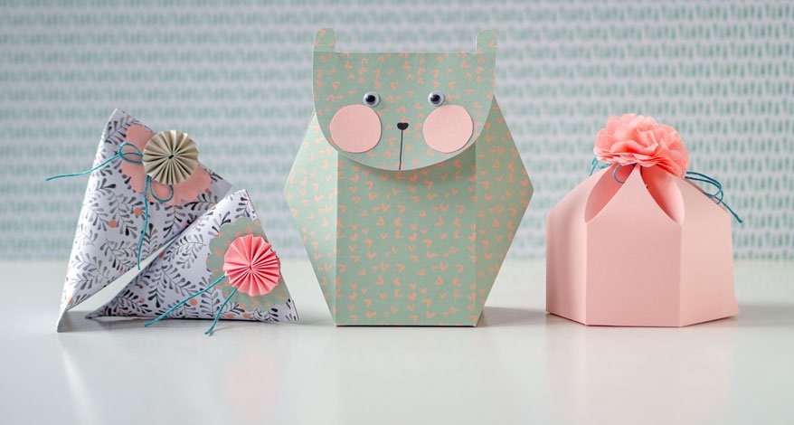 3 selbstgebastelte Geschenschachten aus Papier in Pastellfarbe stehen nebeneinander.