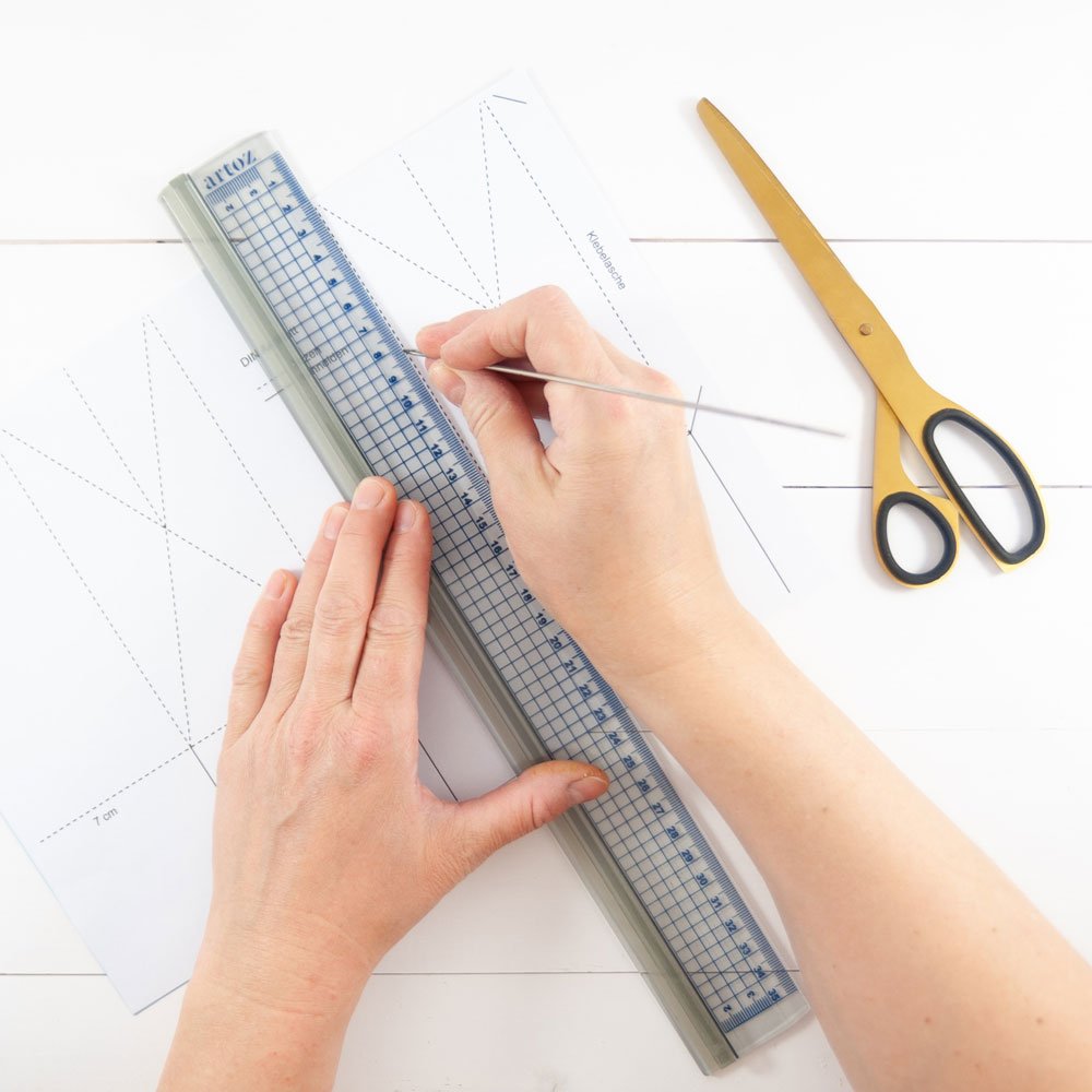 Zwei Hände übertragen mit Hilfe eines Lineals Striche von einer Bastelvorlage auf Papier.