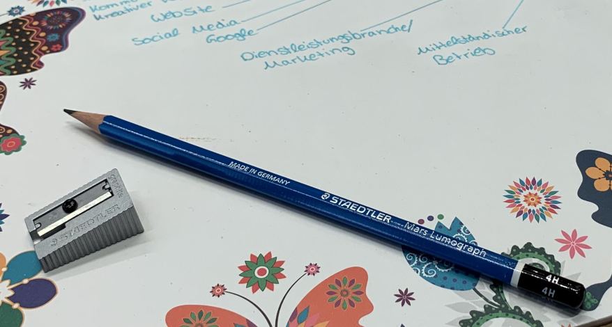 Bleistift und Spitzer auf bunter Mindmap mit Blumen und Schmetterlingen