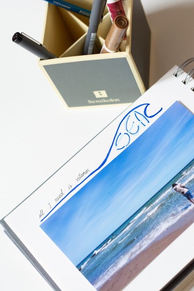 Eine Seite des Ringbuchs der Marke Semikolon ist mit einem Urlaubsbild vom Strand beklebt. Darüber steht gelettert der Spruch "all you need is vitamin sea". Neben dem Ringbuch steht ein Stifteköcher der Marke Semikolon mit diversen Stiften.