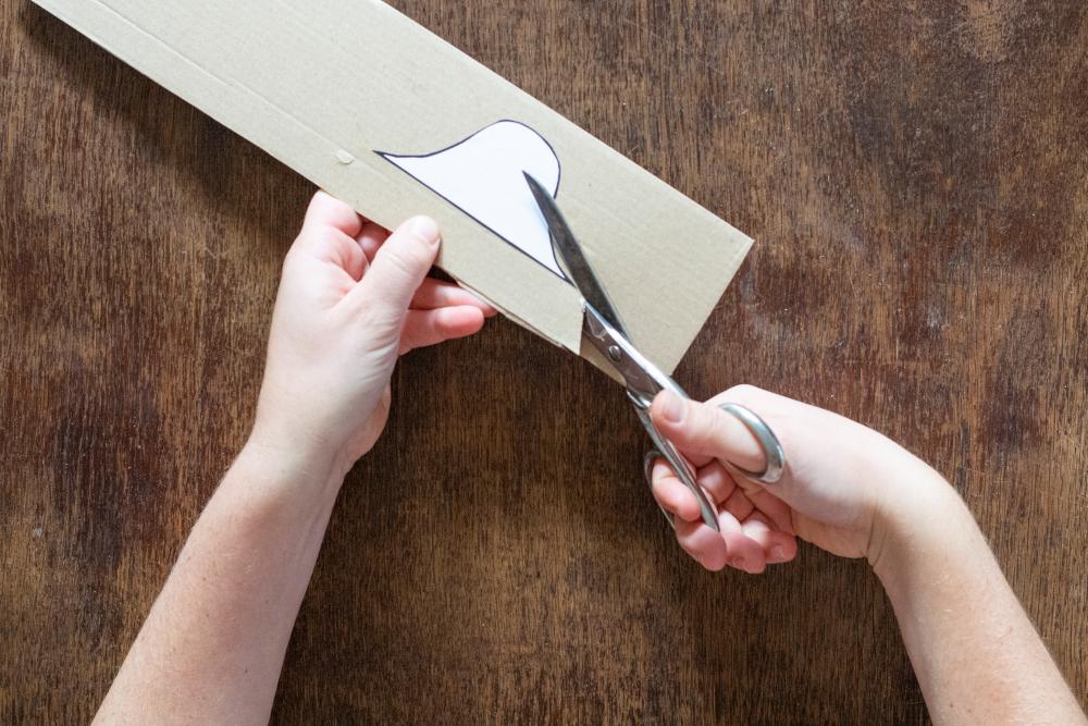 Eine Hand hält den Karton mit der Schblone fest, die andere Hand schneidet die Schablone aus.