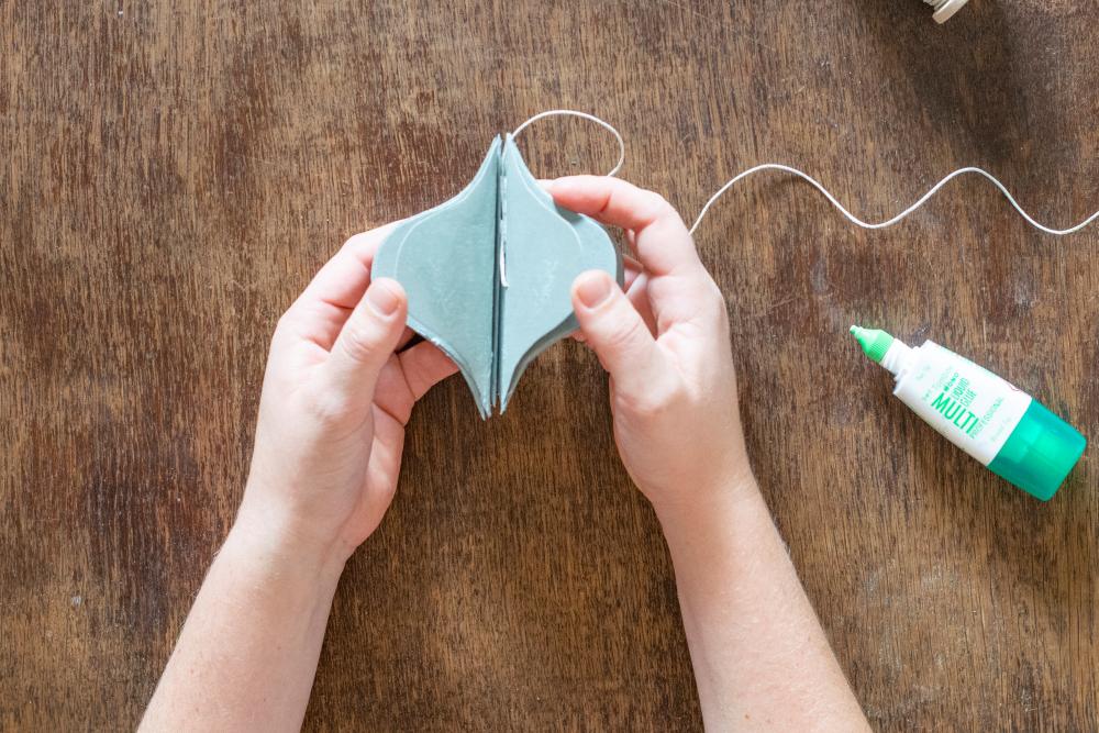 Zwei Hände kleben die Papierlemente zu einer Kugel zusammen. Auf dem Holztisch liegt eine Tube Flüssigklebstoff.