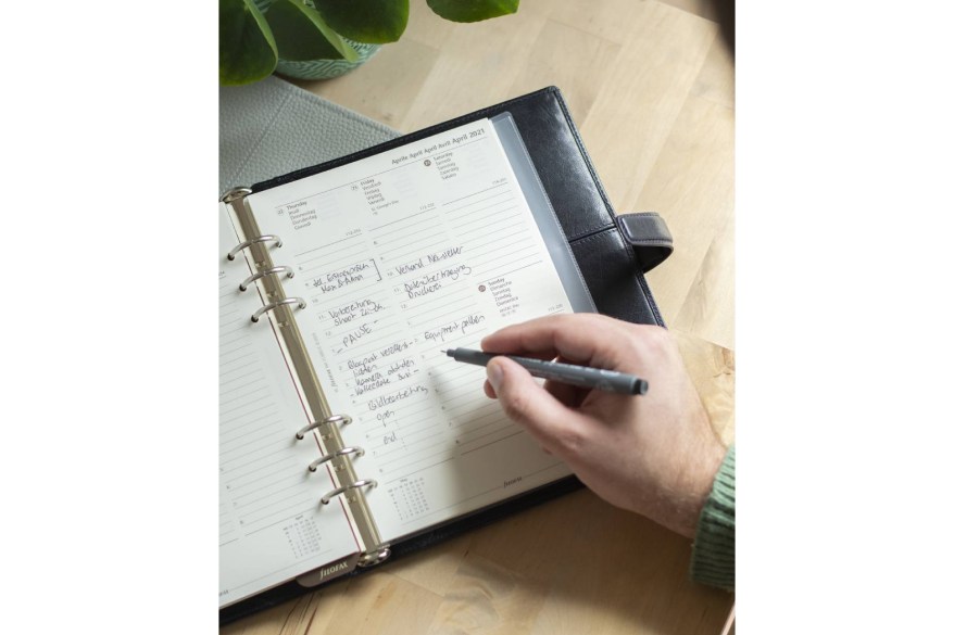 Jemand trägt Notizen in einen aufgeschlagenen Kalender ein.